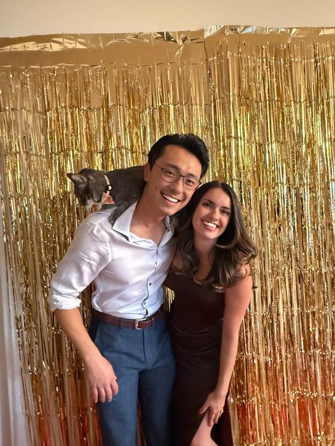 A party photo with a gold backdrop and a cat on one shoulder